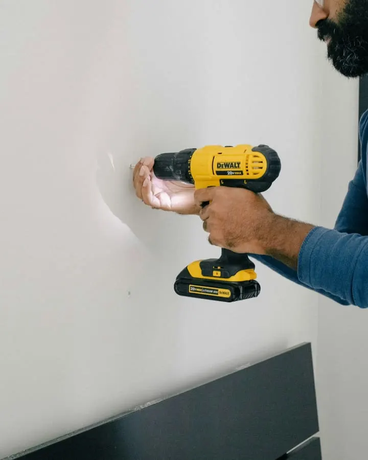 Persona perforando una pared de placa de roca de yeso con un taladro sin percusión