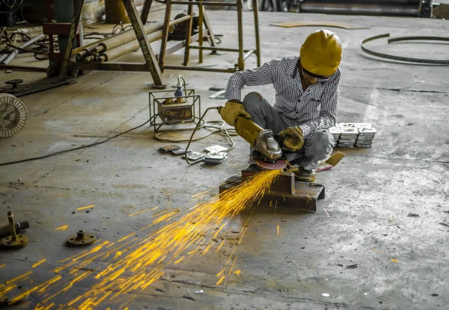 Trabajador usando una amoladora angular sobre una pieza metálica, con chispas saltando