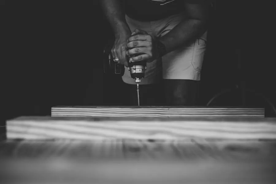 Persona atornillando una tabla de madera con un taladro eléctrico